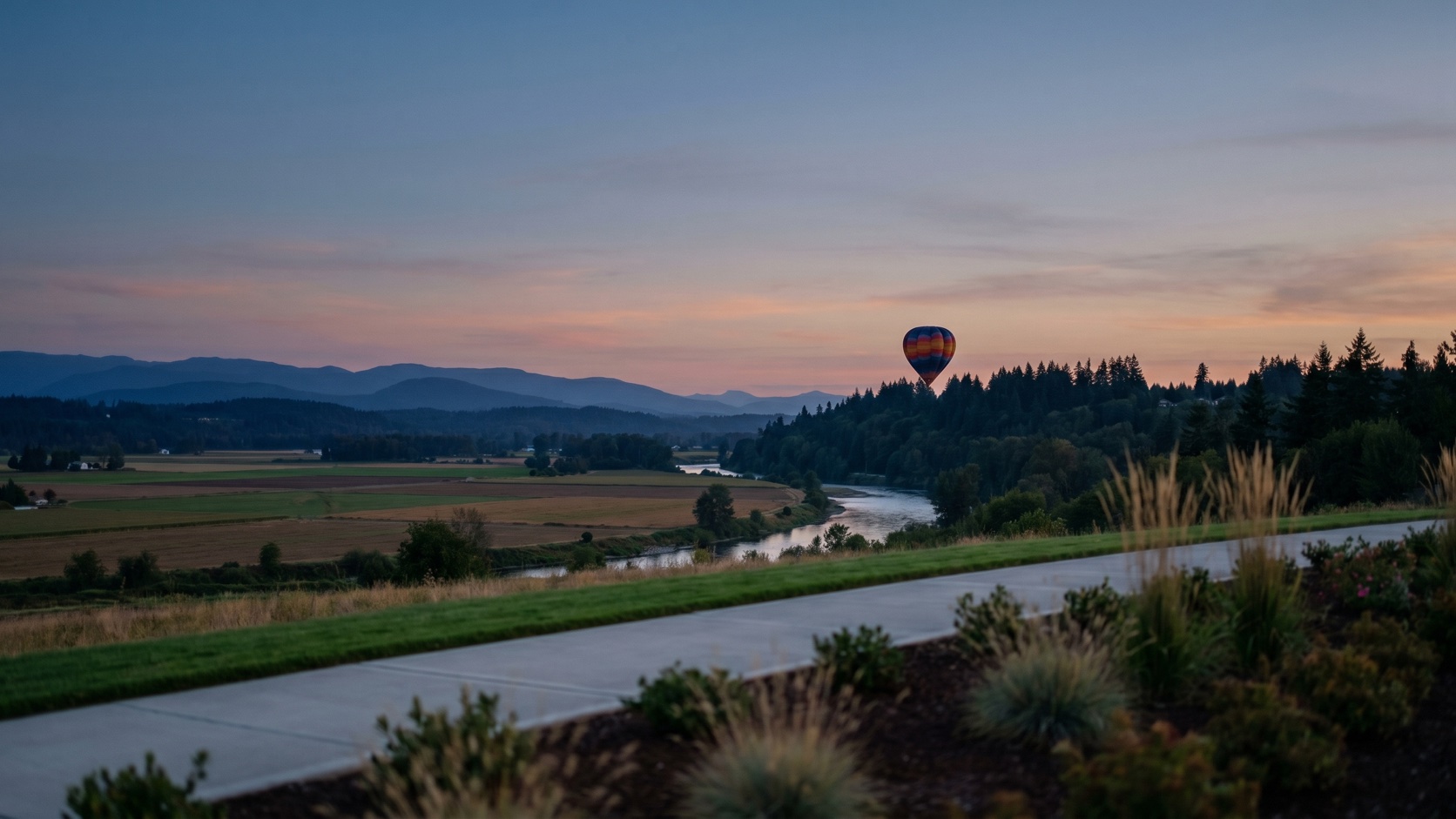 Soft dusk view across the Snohomish River Valley farmland with a hot air balloon drifting above the evergreen treeline